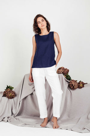 Minimalist summer outfit featuring a navy linen cropped top and white linen trousers, worn barefoot by a model standing against a soft grey-toned background.