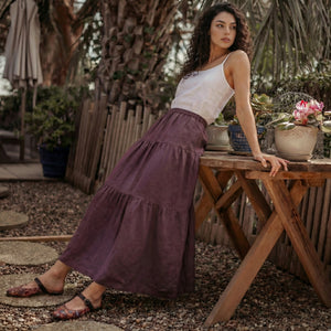 Woman leaning on a wooden table outdoors wearing a breathable grape wine linen skirt for summer.