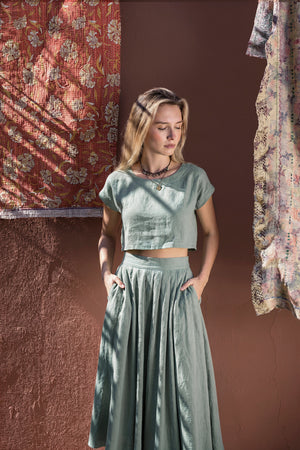 Model with hands in her pockets showcasing the relaxed fit of the NAOMI dusty sage linen two-piece set, featuring a high-waisted midi skirt and boxy crop top.