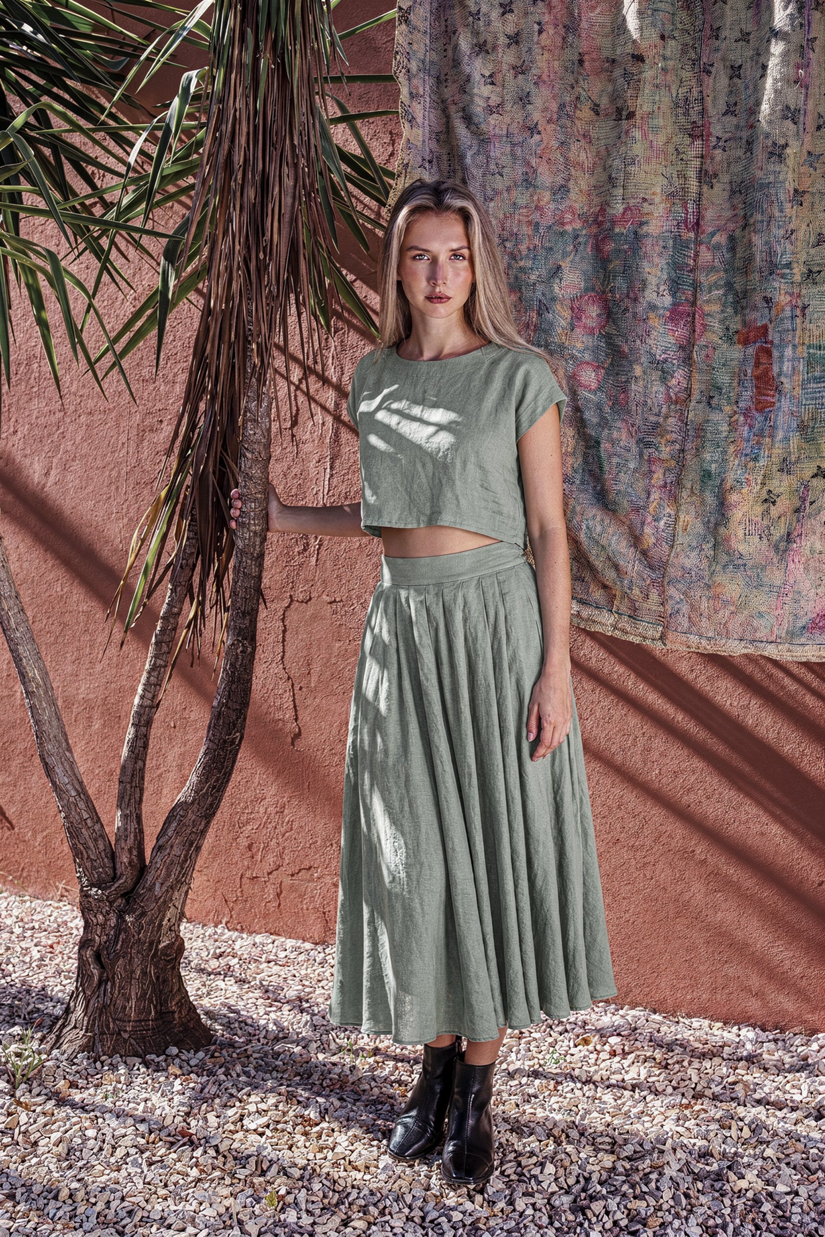 Model posing next to a tree wearing the NAOMI dusty sage linen two-piece dress set, featuring a relaxed boxy crop top and high-waisted midi skirt.