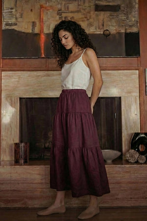 Woman wearing a grape wine linen midi skirt with a tiered design and elastic waist, standing in a modern living room.