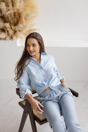 Model wearing dusty blue linen pants, sitting comfortably with legs crossed, demonstrating the versatile and laid-back style of the pants.