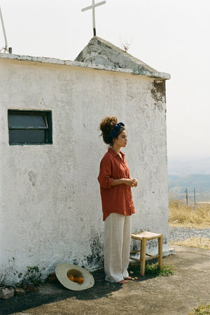 Full-length view of the SOFIJA oversized linen shirt in Clay, showing the relaxed fit and long sleeve drape with white linen pants.