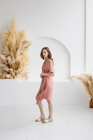 Woman wearing a blush salmon linen wrap dress with a belted waist, V-neckline, and short sleeves. A versatile, breathable, medium-weight linen dress, perfect for casual and summer wear.