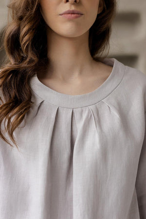 Close-up of the softly rounded neckline with subtle pleats on the grey Calyra linen tunic.