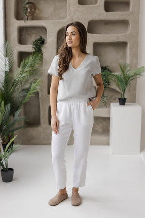 Woman standing with hands in pockets, modeling a relaxed-fit linen blouse with a flattering silhouette in a neutral color.