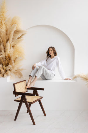 Model seated on ledge, wearing dusty gray straight-leg linen pants and white blouse, casual summer wear.