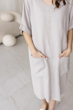 Detailed close-up of light gray linen fabric, highlighting the dress's deep front pockets and breathable, textured material. Sustainable and stylish for casual wear.