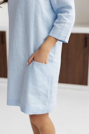Close-up of light blue linen shift dress, showing front pockets and linen fabric texture.