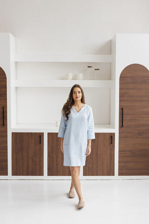 Light blue linen shift dress on a woman, relaxed fit, in a white and wood minimalist room.