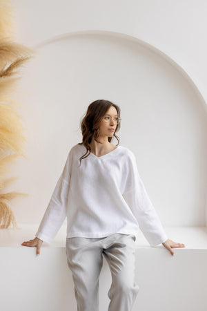 Model seated against arch, wearing dusty gray straight-leg linen pants with elastic waist and white top.