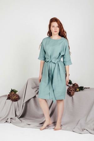 Full-body studio shot of a model wearing the LIRA sea-green linen tunic dress by Sonfre, demonstrating the relaxed fit, tied waist, and boat neckline.