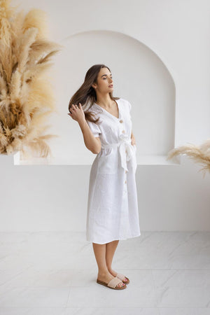 Model in a handmade white linen sundress with a flattering A-line cut, wooden buttons, and puff sleeves, styled for warm weather.