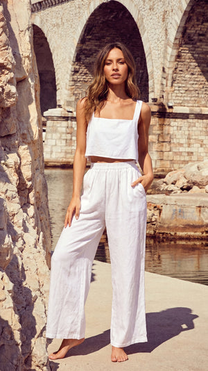 Model standing by a historic stone archway wearing the TORA white linen cropped top with wide-set shoulder straps.