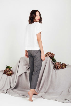Side view of woman modeling SORA relaxed-fit white linen blouse and grey trousers