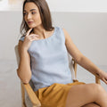 Close-up of a woman in a sleeveless dusty blue linen blouse with mustard shorts, showcasing natural fabric and boho summer vibes.