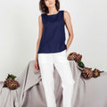 Minimalist summer outfit featuring a navy linen cropped top and white linen trousers, worn barefoot by a model standing against a soft grey-toned background.