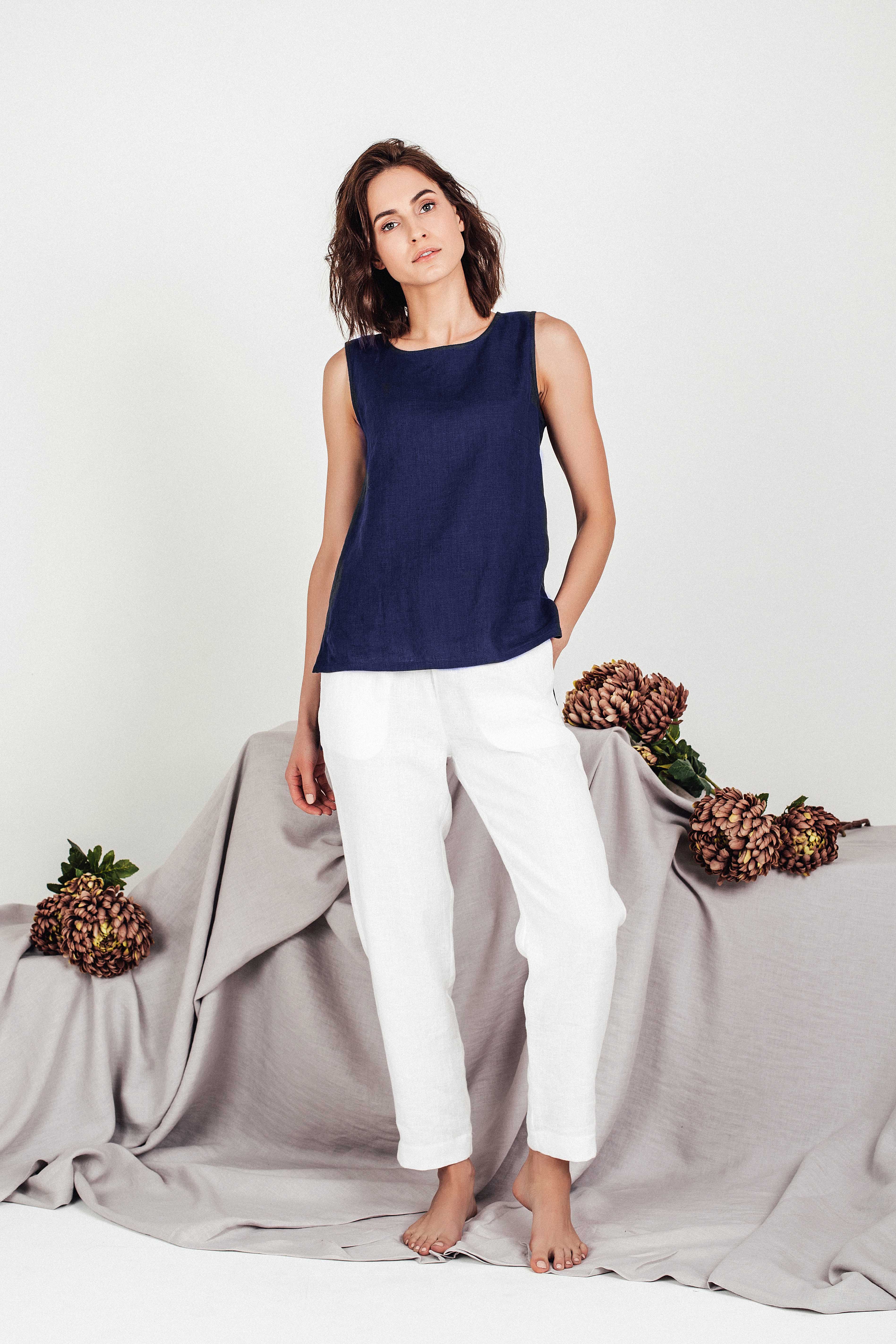 Minimalist summer outfit featuring a navy linen cropped top and white linen trousers, worn barefoot by a model standing against a soft grey-toned background.