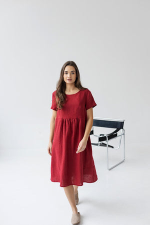 Model standing in a burgundy red linen maternity dress, showcasing the relaxed fit and scoop neck design.
