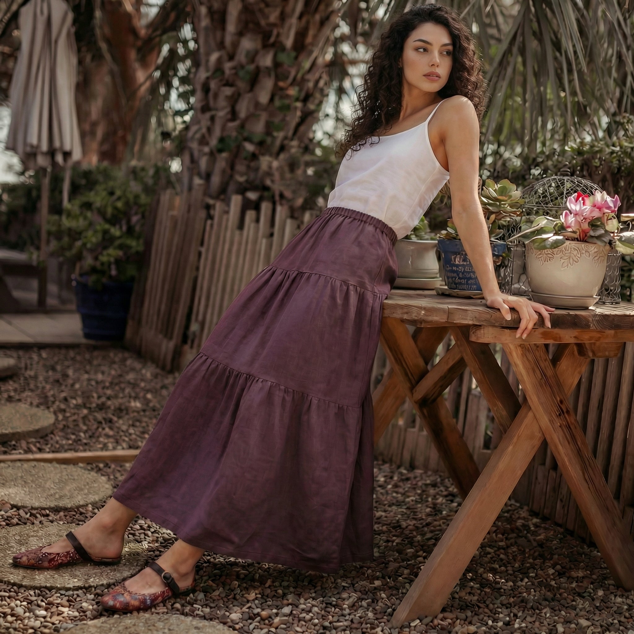 Woman leaning on a wooden table outdoors wearing a breathable grape wine linen skirt for summer.