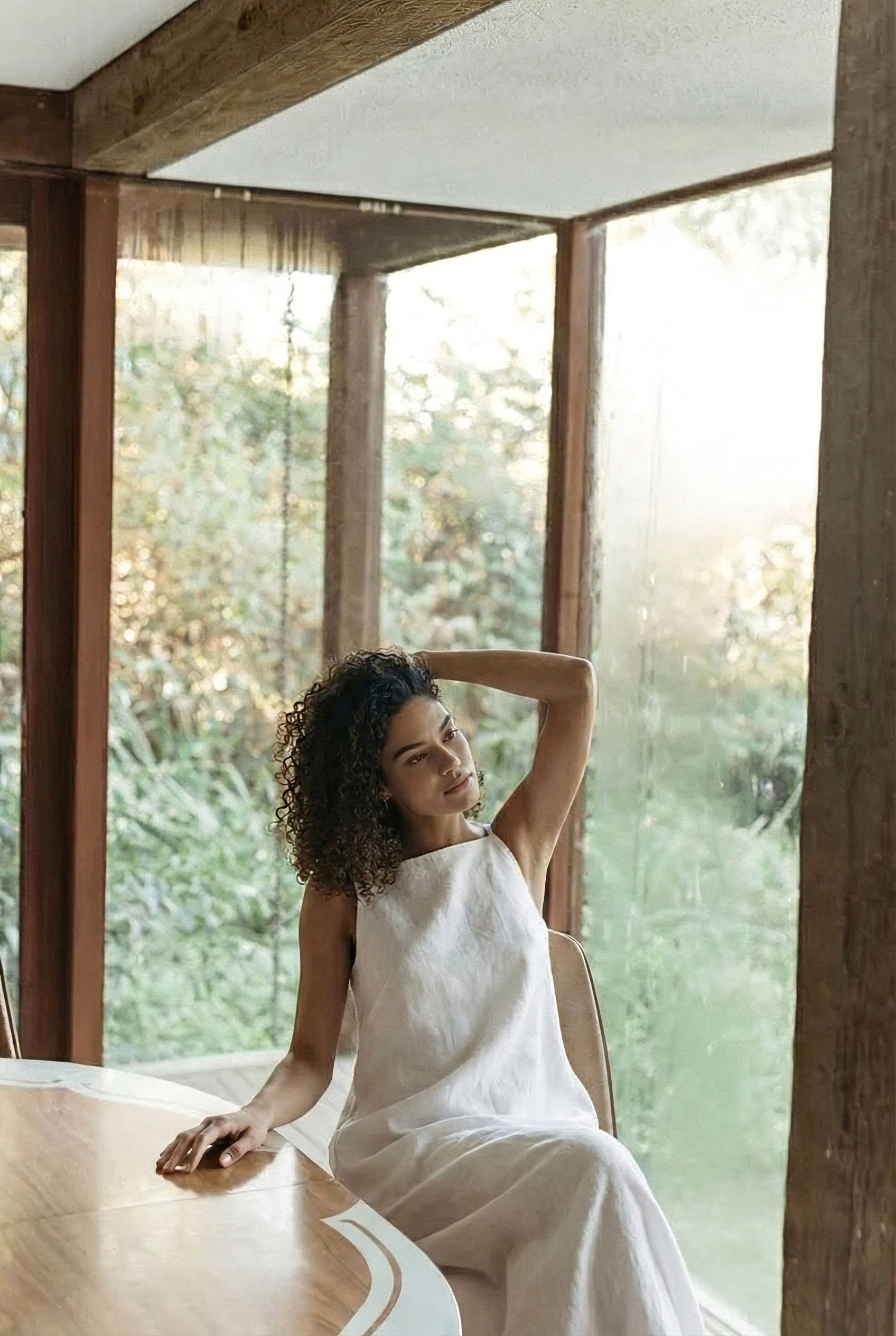 Woman relaxing in armchair wearing soft, hypoallergenic white linen maxi dress.