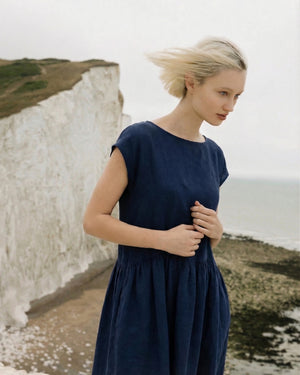 Detail shot of the bodice and neckline of a midnight blue linen smock dress worn by a blonde model outdoors.