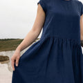 Close-up of a woman holding out the skirt of the Daiva midnight blue linen smock dress from the 2026 collection, showcasing the natural drape and volume of the gathered fabric.