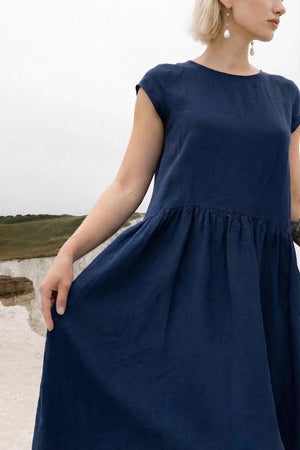 Close-up of a woman holding out the skirt of the Daiva midnight blue linen smock dress from the 2026 collection, showcasing the natural drape and volume of the gathered fabric.
