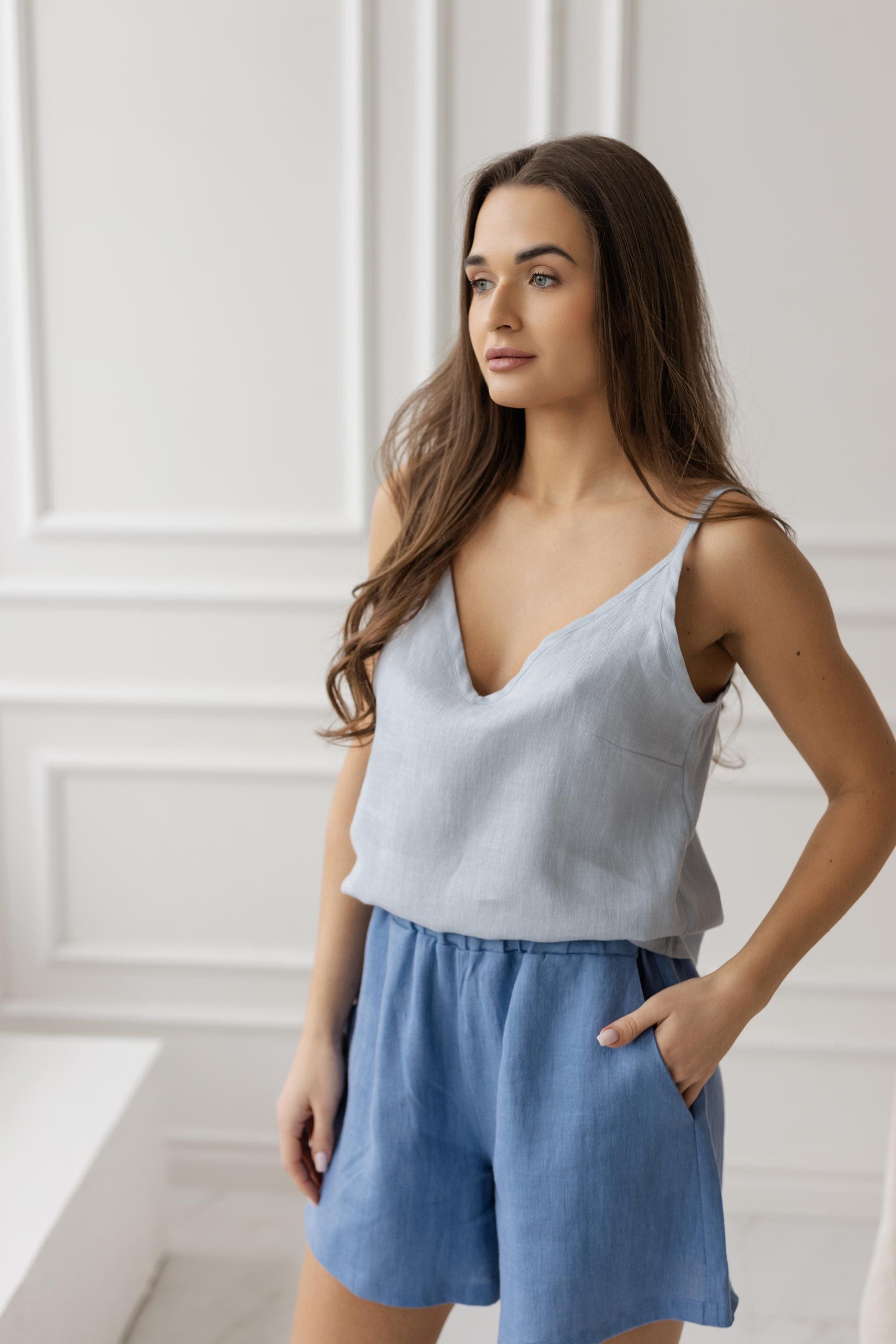 Model styled in denim blue linen shorts, a light blue camisole, and a coordinating light blue button-up shirt, presenting a casual yet chic summer look.