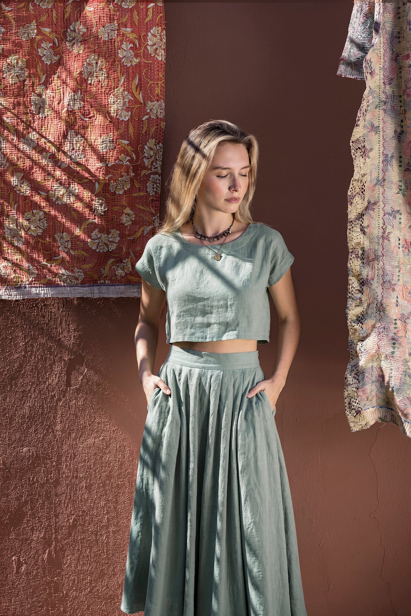 Model with hands in her pockets showcasing the relaxed fit of the NAOMI dusty sage linen two-piece set, featuring a high-waisted midi skirt and boxy crop top.