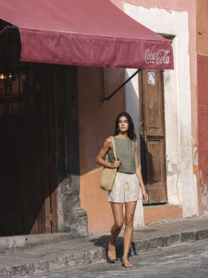 Model wearing the VIDA eucalyptus green sleeveless linen crop top by SONFRÉ in a casual summer street-style look.