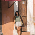 Model wearing the VIDA eucalyptus green sleeveless linen crop top by SONFRÉ, paired with striped linen shorts.