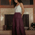 Woman wearing a grape wine linen midi skirt with a tiered design and elastic waist, standing in a modern living room.
