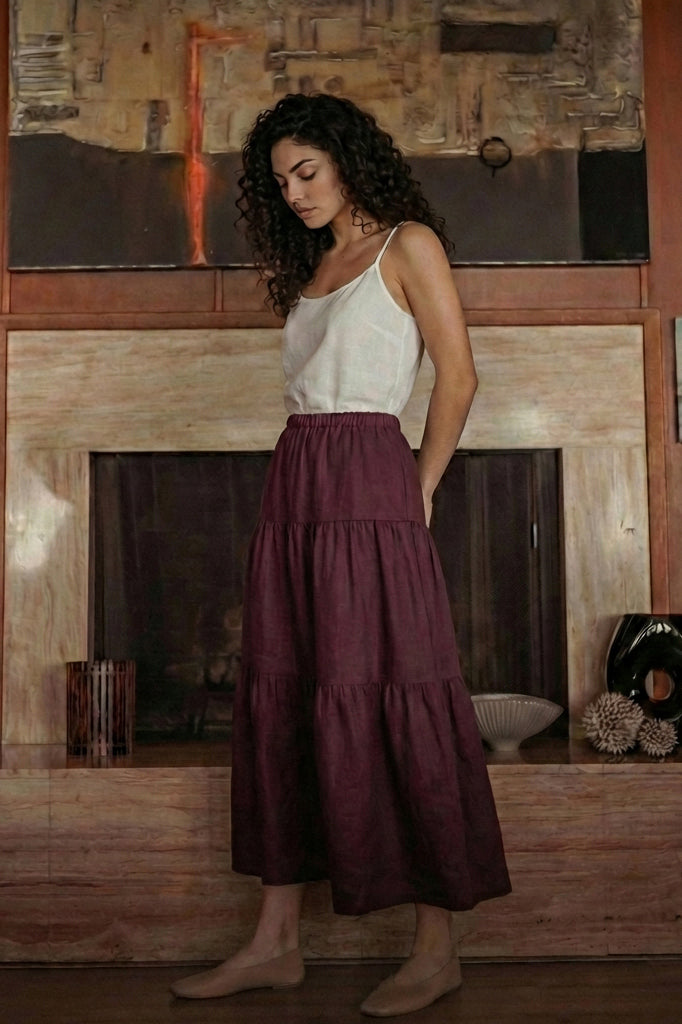 Woman wearing a grape wine linen midi skirt with a tiered design and elastic waist, standing in a modern living room.