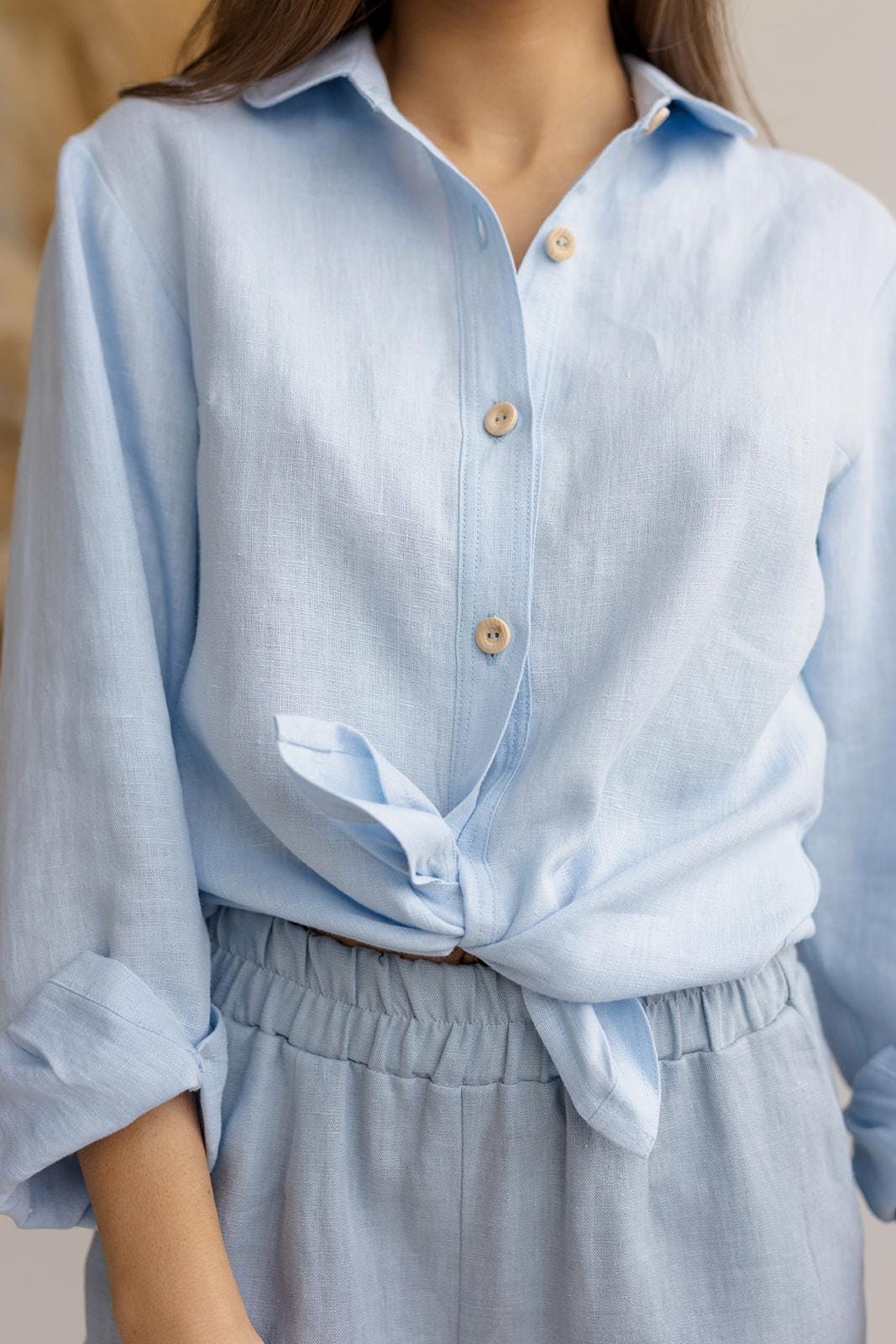 Close-up of breathable linen fabric and collared neckline, ice blue button-down shirt, wooden buttons.