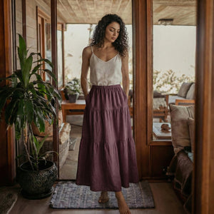 Woman wearing a grape wine linen tiered skirt with functional deep side pockets.