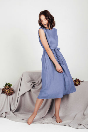 Model looking downward while wearing the LINUVA denim blue linen midi dress by SonFre, showcasing the tie belt and the flowing drape of the A-line skirt.