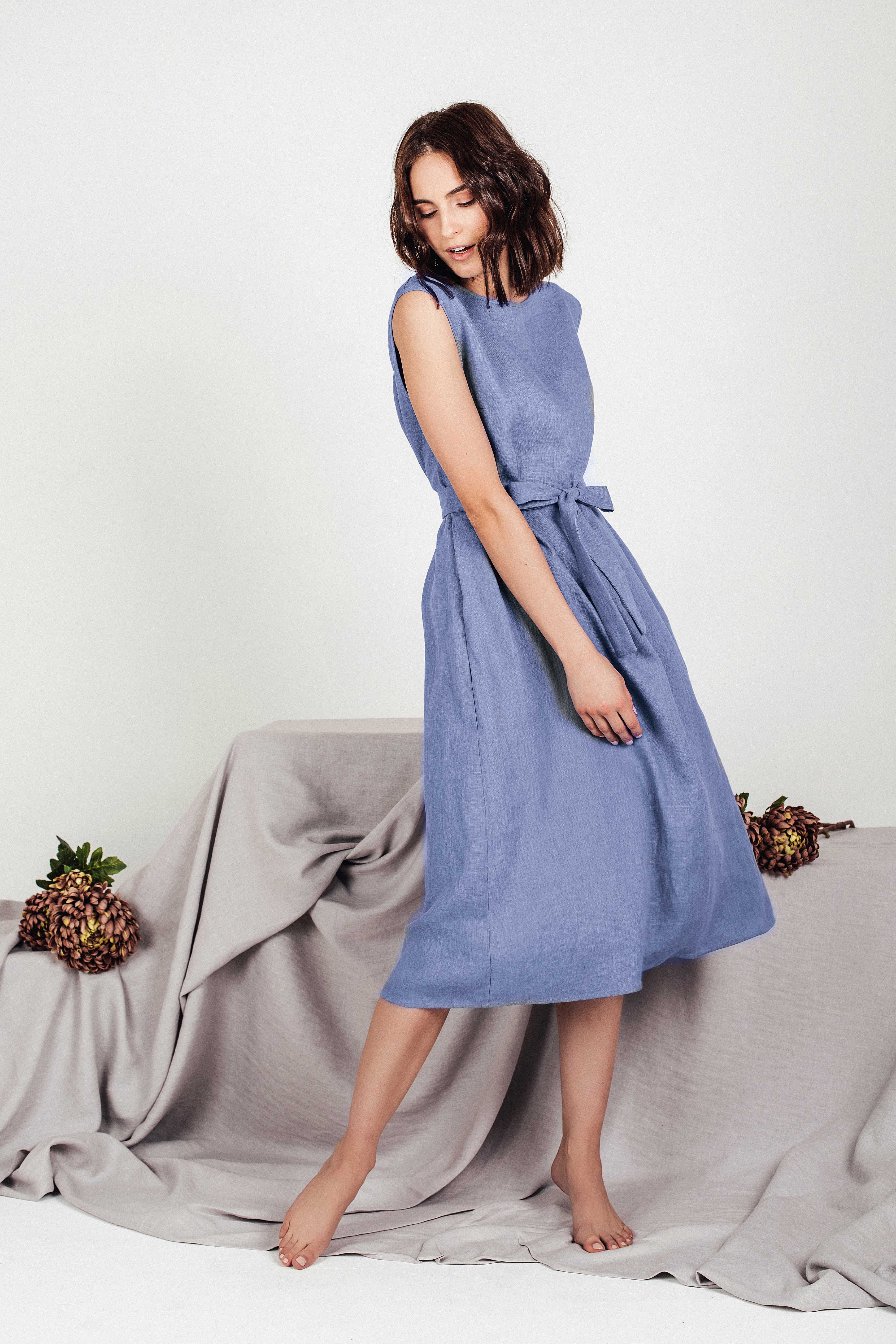 Model looking downward while wearing the LINUVA denim blue linen midi dress by SonFre, showcasing the tie belt and the flowing drape of the A-line skirt.