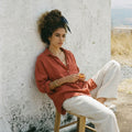 Model wearing the SOFIJA oversized long sleeve linen shirt in Clay, paired with white linen trousers.