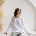 Woman wearing the Solvia white medium weight linen blouse, relaxed V-neck fit, in minimalist studio.
