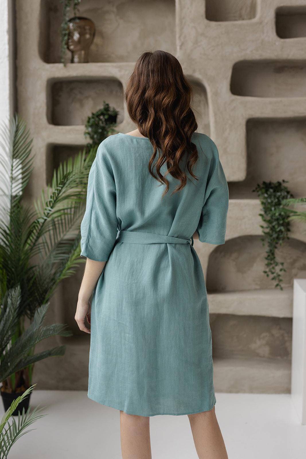 Back view of knee-length linen tunic dress, adjustable belted waist, breathable fabric, three-quarter sleeves.