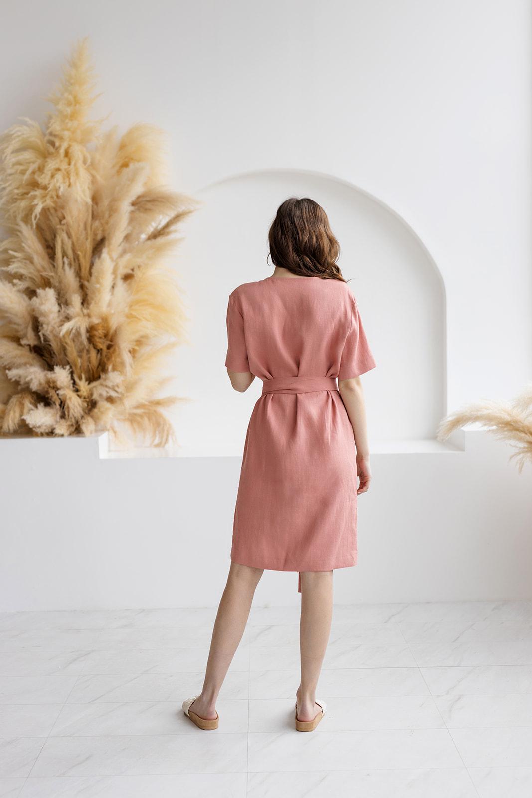 Back view of a blush salmon linen wrap dress, featuring a knee-length design, a fabric tie belt, and a relaxed fit. Crafted from high-quality, breathable linen for everyday elegance.