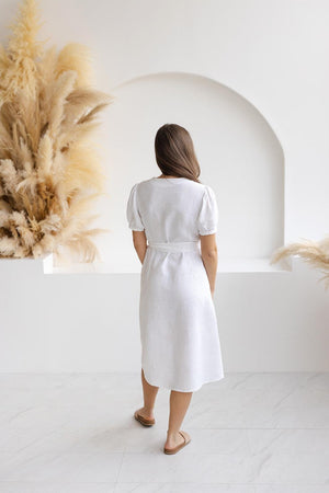 Back view of model wearing a white linen midi dress with short puff sleeves and a tie belt, highlighting the lightweight fabric and relaxed fit