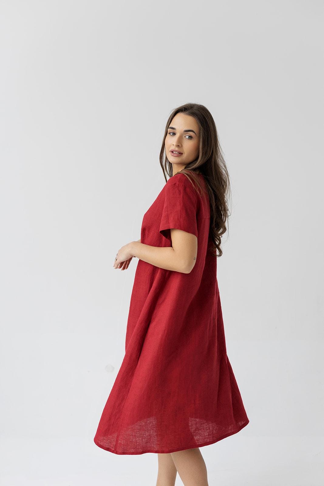 Side view of a woman in a burgundy red linen maternity dress with a loose fit and soft pleats.