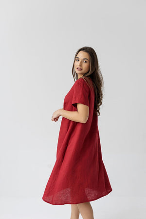 Side view of a woman in a burgundy red linen maternity dress with a loose fit and soft pleats.