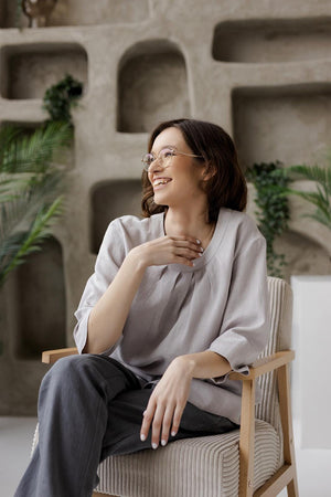 Seated model wearing the Calyra gray linen tunic, illustrating the comfortable 3/4 sleeves and relaxed silhouette.