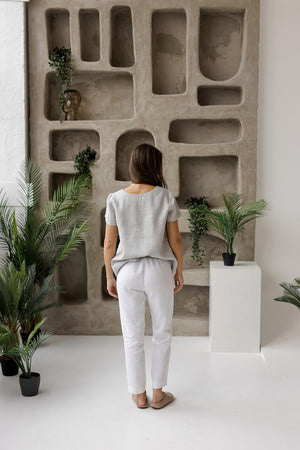 Rear view of a woman in a dusty gray linen blouse, showcasing its minimalist design, breathable fabric, and relaxed drape.