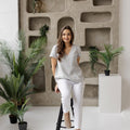 Woman sitting on a black stool, wearing a lightweight linen blouse in dusty gray, styled for a casual yet refined look.