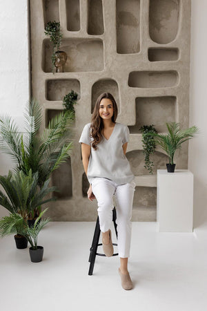 Woman sitting on a black stool, wearing a lightweight linen blouse in dusty gray, styled for a casual yet refined look.