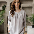 Closer front shot of the Calyra gray linen tunic, highlighting the round neckline with delicate pleats.